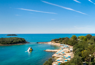 Panoramabillede af Valamar Camping Istra i Istrien, Kroatien med strand, blå paraplyer og klart havvand.