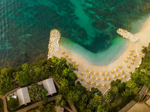 Vista aérea de Valamar Camping Istra en Croacia, con mar azul, playa de guijarros y sombrillas alineadas.
