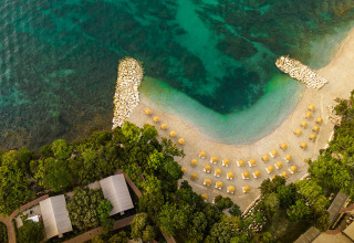 Vista aerea del Valamar Camping Istra in Croazia con spiaggia di ciottoli, ombrelloni e mare cristallino.