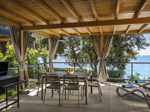 Overdekt terras bij Marbello Suite met eettafel, ligstoelen, gordijnen en uitzicht op zee.