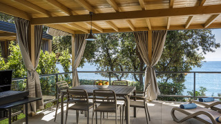 Overdekt terras bij Marbello Suite met tuinset, ligstoelen, gordijnen en zicht op de zee.