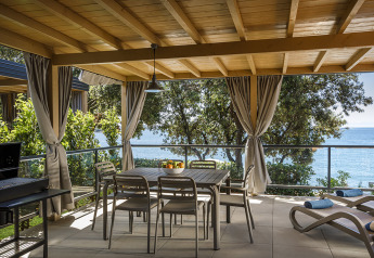 Udendørs terrasse i Marbello Suite med spisebord, havudsigt, liggestole og gardiner under et træloft.