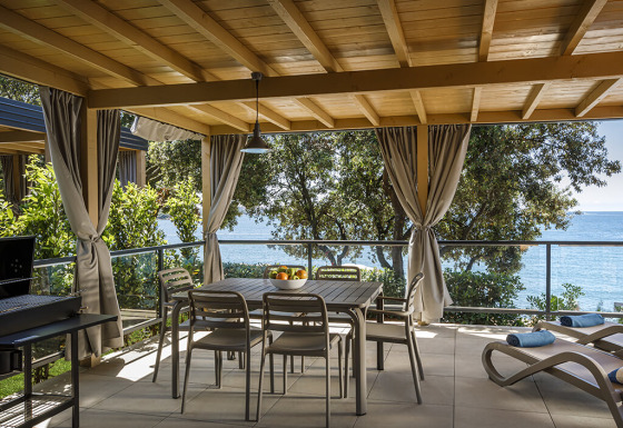 Overdekt terras bij Marbello Suite met eettafel, ligstoelen, gordijnen en uitzicht op zee.