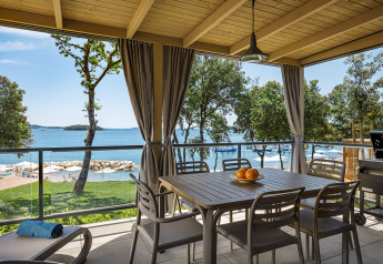 Terrasse couverte avec table à manger et chaises, vue sur la mer avec arbres et plage en arrière-plan.