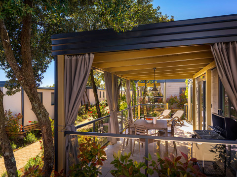 Overdekt terras bij Bella Vista Home-lodge met tafel, ligzetels, barbecue en tuinzicht.