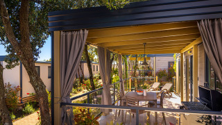 Overdekt terras bij Bella Vista Home-lodge met tafel, ligzetels, barbecue en tuinzicht.