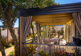 Overdekt terras bij Bella Vista Home-lodge met tafel, ligzetels, barbecue en tuinzicht.
