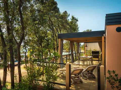 Terraza de una cabaña rodeada de árboles con tumbonas, mesa de comedor y ambiente tranquilo.