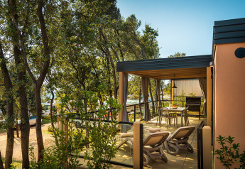 Terrasse de lodge entourée d’arbres, avec chaises longues, table à manger et atmosphère paisible.