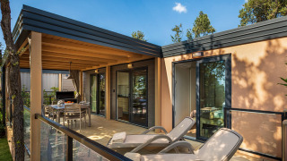 Buitenterras aan een lodge met ligstoelen, eetruimte en glazen leuning omgeven door bomen.