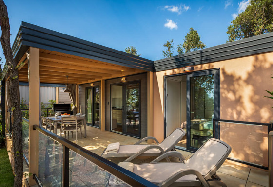Buitenterras aan een lodge met ligstoelen, eetruimte en glazen leuning omgeven door bomen.