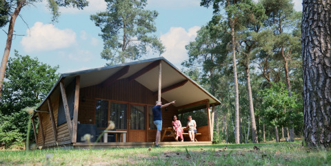 Familie entspannt vor einem Safarilodge deluxe Safarizelt in einem sonnigen, bewaldeten Gebiet.