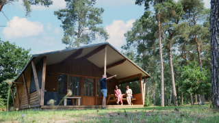 Famiglia che si rilassa davanti a una tenda Safarilodge deluxe in una foresta soleggiata.