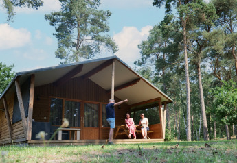 Famiglia che si rilassa davanti a una tenda Safarilodge deluxe in una foresta soleggiata.