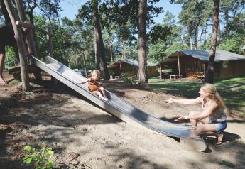 Una madre aspetta il suo bambino che scende dallo scivolo vicino alle tende safari al Familievakantiepark Krieghuusbelten.