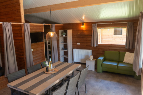 Intérieur de la Safarilodge deluxe au Familievakantiepark Krieghuusbelten avec table et canapé verts.