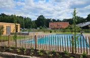 Vista di una piscina, recinzione in legno e case a Camping Dal van de Mosbeek, Overijssel, Paesi Bassi.