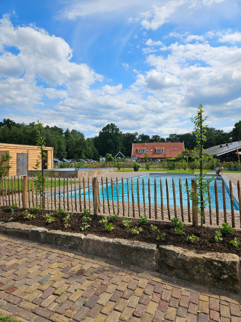 Vista di una piscina, recinzione in legno e case a Camping Dal van de Mosbeek, Overijssel, Paesi Bassi.
