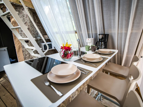Cuisine moderne avec comptoir repas, quatre couverts, cafetière, mugs et fleurs dans une tente safari.