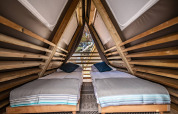 Intérieur d’une tente safari avec deux lits simples et structures en bois sous un toit en triangle.