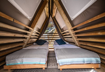 Interno di una tenda safari con due letti singoli e pareti in legno sotto un tetto a spiovente.