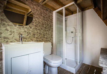 Safari tent bathroom featuring a wooden ceiling, shower cabin, toilet, sink, and a round mirror on the wall.