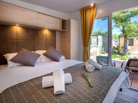 Camera di lodge moderna con letto matrimoniale, cuscini, asciugamani arrotolati e vista terrazza sul giardino.