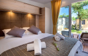 Camera di lodge moderna con letto matrimoniale, cuscini, asciugamani arrotolati e vista terrazza sul giardino.