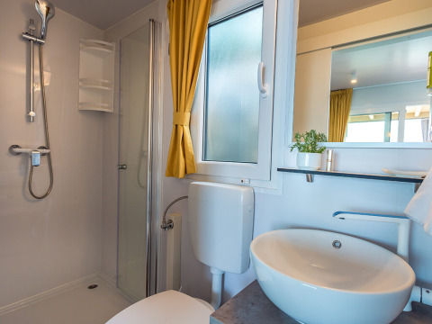 Modern lodgebadkamer met douche, wit wastafel, toilet, gele gordijnen, matglasraam en spiegel.