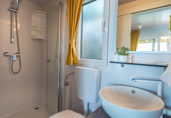 Moderne lodgebadeværelse med bruser, hvid vask, toilet, gul gardin og et vindue med matteret glas.
