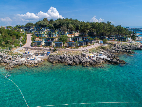 Kystudsigt over et moderne ferielodgekompleks bygget på klipper ved det klare blå hav under blå himmel.
