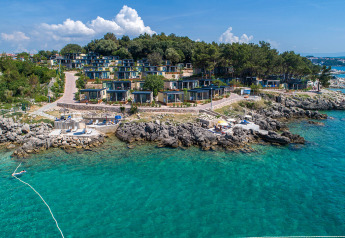 Kystudsigt over et moderne ferielodgekompleks bygget på klipper ved det klare blå hav under blå himmel.