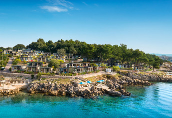Moderne lodges op een heuvel aan de kust, tussen groen en helderblauw water, met rotsachtige oevers.