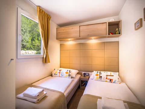Moderne lodgekamer met twee eenpersoonsbedden, beige hoofdbord, raam en houten opbergplanken boven.