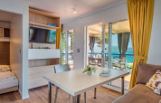 Lodge moderne avec table à manger, canapé, rideaux jaunes et vue sur la mer par de grandes portes vitrées.