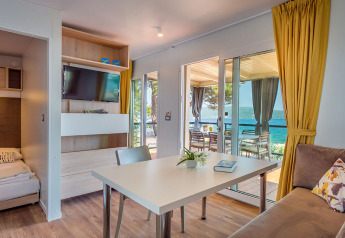 Lodge moderno con tavolo da pranzo, divano, tende gialle e vista mare attraverso grandi porte a vetri.