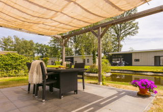 Gezellige overdekte zithoek met uitzicht op het water en moderne chalets in vakantiepark De Lochemse Berg.