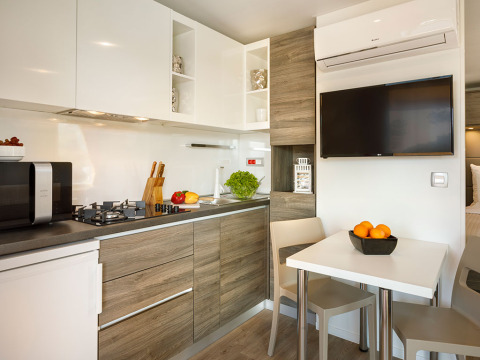Coin cuisine et salle à manger modernes avec armoires en bois, TV et fruits, Lungomare Chalet en Croatie.