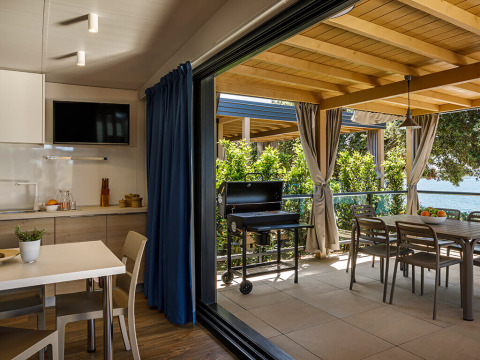 Moderne eethoek en keuken met terras, barbecue en zeezicht, omringd door volop groene planten.