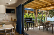 Moderne eethoek en keuken met terras, barbecue en zeezicht, omringd door volop groene planten.
