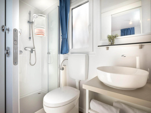 Modern en compact lodge-badkamer met douche, toilet, grote wastafel, raam en opgerolde handdoeken.