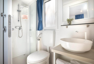 Modern en compact lodge-badkamer met douche, toilet, grote wastafel, raam en opgerolde handdoeken.