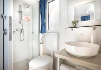 Salle de bain moderne et compacte dans un lodge, avec douche, toilettes, lavabo et fenêtre lumineuse.