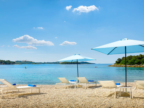 Ligbedden met blauwe parasols aan het strand van Marbello Home, Valamar Camping Istra, Kroatië, in de zon.