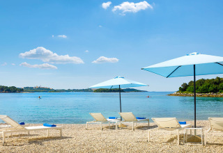 Ligbedden met blauwe parasols aan het strand van Marbello Home, Valamar Camping Istra, Kroatië, in de zon.