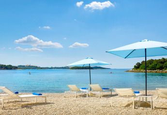 Ligbedden met blauwe parasols aan het strand van Marbello Home, Valamar Camping Istra, Kroatië, in de zon.