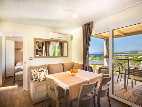 Moderne lodge woonkamer met eetruimte, sofa en balkon met uitzicht op zee en het landschap buiten.