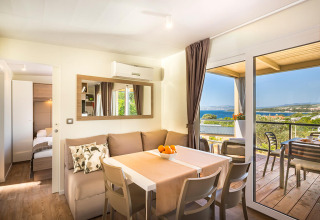 Moderne lodge woonkamer met eetruimte, sofa en balkon met uitzicht op zee en het landschap buiten.
