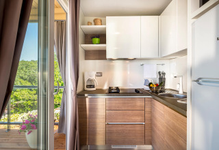 Moderne keuken in een lodge met houten kasten, witte planken en uitzicht op het groen buiten via de deur.