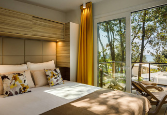 Chambre de lodge moderne avec coussins, rideaux jaunes et balcon surplombant les arbres et la mer.